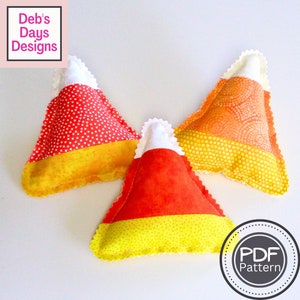 May include: Three handmade felt candy corn pillows in orange, yellow, and white with a polka dot pattern. The pillows are shaped like candy corn and have a scalloped edge. The text "PDF Pattern" is visible in the lower right corner of the image.