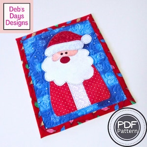 May include: A red and white Santa Claus applique with a blue background. The applique is surrounded by a red border with a white polka dot pattern. The background fabric has a blue and white pattern of snowflakes and Christmas lights. The text "PDF Pattern" is visible in a circle in the lower right corner of the image.