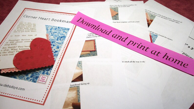 May include: A pink paper strip with the text "Download and print at home" on it. The paper strip is on top of a white sheet of paper with instructions for making a corner heart bookmark. The instructions include a diagram of a heart shape and the text "Corner Heart Bookmark".