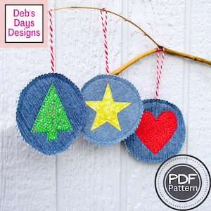 Pode incluir: Três enfeites de ganga com cordas vermelhas e brancas para pendurar. Um tem uma árvore verde, outro uma estrela amarela e o último um coração vermelho. Os enfeites estão pendurados num galho. O texto "Deb's Days Designs" é visível.