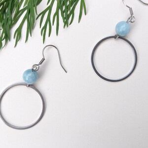 Könnte beinhalten: Ein Paar silberne Creolen mit einer hellblauen Edelsteinperle an jedem Ohrring.