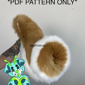 Puede incluir: Una cola peluda marrón y blanca con una textura esponjosa. El texto "*PDF PATTERN ONLY*" está en la parte superior. Un perro alienígena de dibujos animados está en la esquina inferior izquierda. El texto "MARTIAN MUTT" está en la cola.