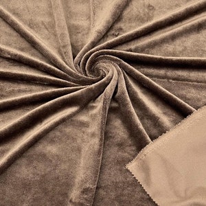 May include: A close-up of a brown plush fabric with a soft, fuzzy texture. The fabric is folded and draped, showcasing its luxurious feel.