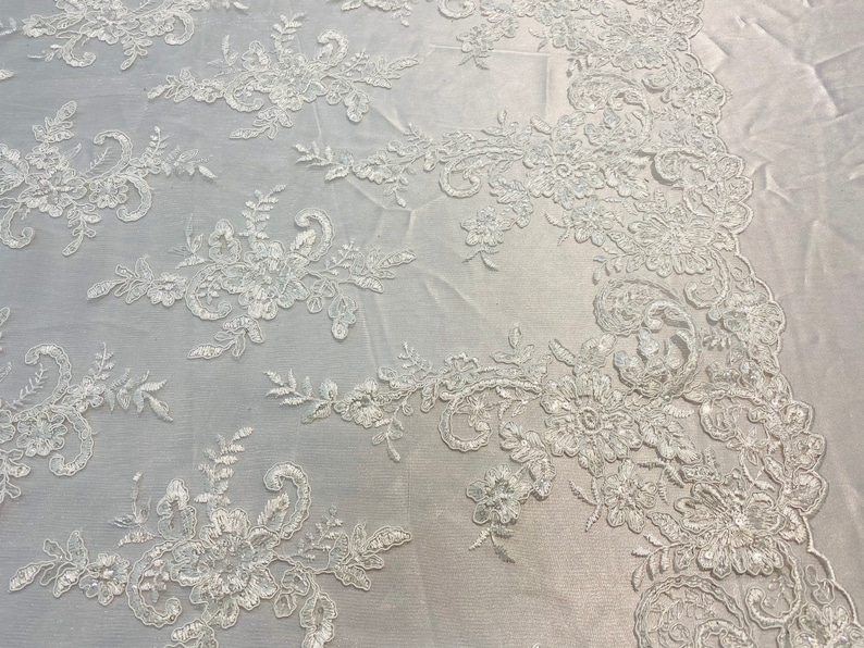 May include: White floral lace fabric with a delicate pattern. The lace is embroidered with small flowers and leaves.