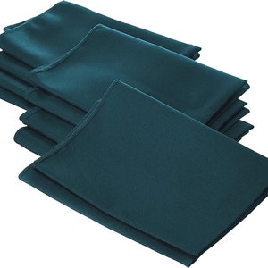 May include: A stack of teal blue napkins folded in a square shape. The napkins are made of a smooth, silky fabric.