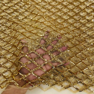 May include: Gold sequined fabric with a diamond pattern. The fabric is sheer and has a delicate texture.