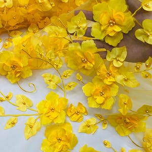 May include: Yellow floral lace fabric with 3D flowers and leaves. The fabric has a delicate mesh background and is embellished with small pearl-like beads.