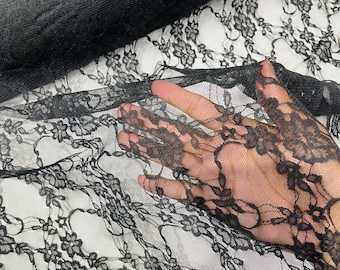 Puede incluir: Tela de encaje negra con un delicado patrón floral. La tela es transparente y tiene una textura suave y fluida.