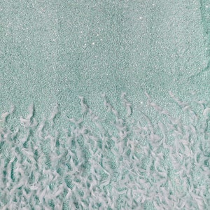 May include: A light blue fabric with a sparkly texture and a fringe of white feathers.