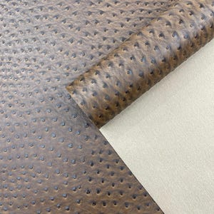 May include: Close-up of brown ostrich leather with a textured surface and small, dark-colored dimples. A portion of the leather is rolled, revealing a beige, smooth backing. The material is suitable for various crafting projects.