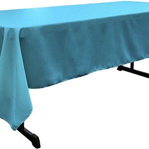 May include: A light blue rectangular tablecloth draped over a table. The tablecloth has a smooth, even texture and hangs down on all sides.