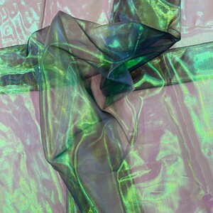 May include: Green and iridescent sheer fabric with a crinkled texture. The fabric is folded and draped, showing the shimmery effect of the material.