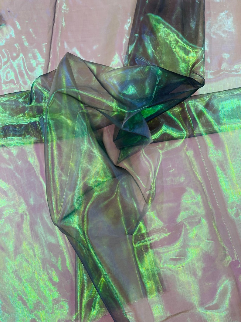 May include: Green and iridescent sheer fabric with a crinkled texture. The fabric is folded and draped, showing the shimmery effect of the material.