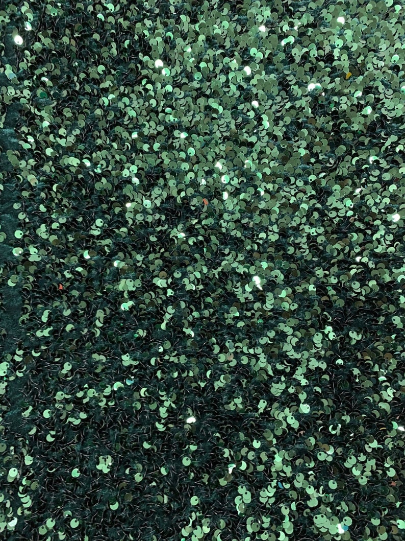 May include: A close-up of a fabric covered in teal green sequins. The sequins are small and round, creating a shimmering effect.