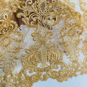 May include: Gold embroidered lace fabric with a delicate floral pattern. The lace is sheer and has a soft, flowing texture.
