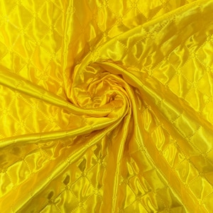 Puede incluir: Tela acolchada de color amarillo brillante con un patrón de diamantes. La tela tiene un aspecto brillante, similar al satén, y está dispuesta en espiral, creando pliegues y sombras. Ideal para acolchado, costura o proyectos de manualidades.