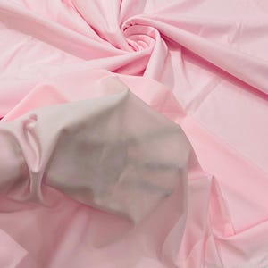 May include: A close-up of a soft, pink fabric. The fabric is smooth and has a slight sheen. It is folded in a way that shows the texture of the material.