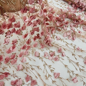 Puede incluir: Tela de encaje floral 3D rosa con purpurina dorada. La tela presenta un delicado patrón floral con flores 3D en relieve.