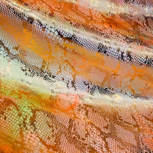 May include: Close-up of a fabric with a snakeskin pattern in shades of orange, gold, and white.