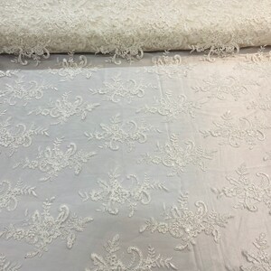 May include: White floral lace fabric with a delicate pattern. The lace is on a sheer mesh background.