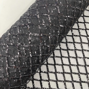 Peut inclure: Un rouleau de tissu noir orné d'un motif quadrillé de sequins argentés. Les sequins forment un motif en losanges sur le tissu sombre. Le tissu roulé révèle la texture et l'éclat du matériau.