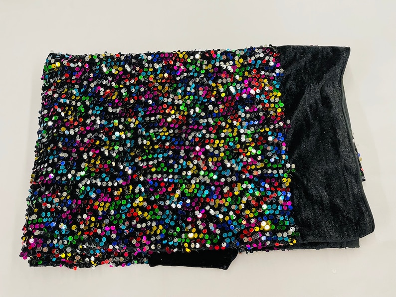May include: A black velvet throw pillow with a colorful sequin design. The sequins are arranged in a random pattern and create a shimmering effect.