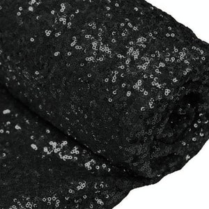 May include: Black sequin fabric with a shiny, sparkly finish. The fabric is folded in half, showing the texture and pattern of the sequins.