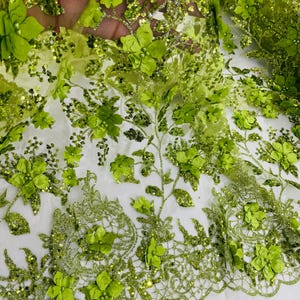 May include: Green floral lace fabric with 3D flowers and sequins. The fabric has a delicate, intricate design and is perfect for adding a touch of elegance to any project.