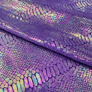 Könnte beinhalten: Nahaufnahme eines leuchtend violetten Stoffes mit Schlangenmuster. Das Material hat eine strukturierte, schillernde Oberfläche mit Anklängen von Regenbogenfarben, die über die Oberfläche schimmern. Der Stoff ist gefaltet und zeigt das detaillierte schuppenartige Design.