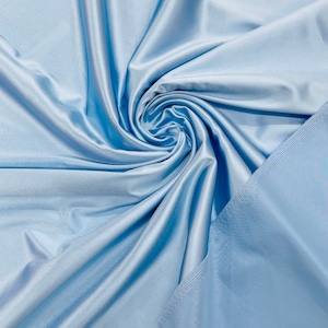 Puede incluir: Una tela sedosa de color azul claro con una textura suave. La tela está doblada y retorcida, creando un patrón de espiral.