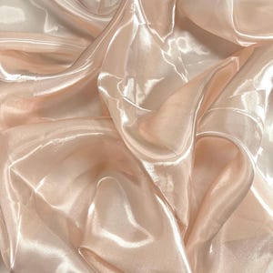 Peut inclure: Gros plan sur un tissu pêche brillant avec des plis doux. Le tissu a un aspect soyeux et fluide, reflétant la lumière et créant des reflets et des ombres. Le matériau semble léger et délicat.
