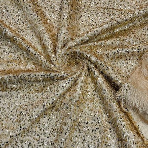 May include: Gold fabric with a fuzzy texture and small sequins. The fabric is folded and draped.