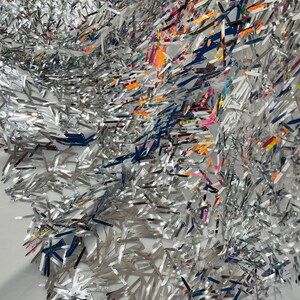 May include: Silver sequins in a variety of shapes and sizes, with some iridescent accents. The sequins are arranged in a random pattern, creating a shimmering and textured effect.