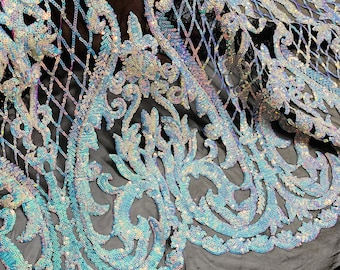 May include: A close-up of iridescent blue and silver sequins sewn onto a black mesh fabric. The sequins are arranged in a floral pattern.