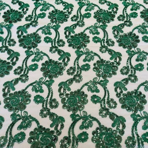 May include: Emerald green floral lace fabric with sequins. The lace features a delicate floral pattern with a scalloped edge.