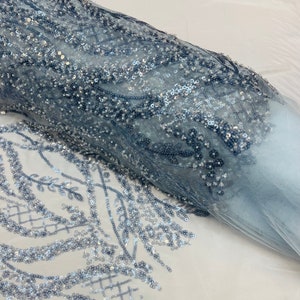 Może przedstawiać: Niebieska tkanina z cekinami w delikatny wzór kwiatowy. Cękiny są rozrzucone na przezroczystej siatce, tworząc mieniący się efekt.