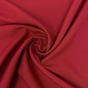 May include: Close-up of a deep red fabric with a smooth, even texture. The fabric is folded and draped, creating soft folds and curves.