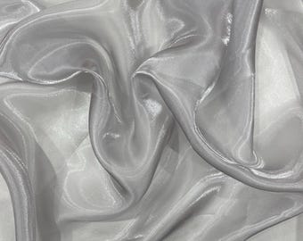 May include: A sheer, light gray fabric with a smooth, reflective surface. The material is draped in soft, flowing folds, creating deep shadows and bright highlights that emphasize its translucent quality and delicate, shimmering texture.