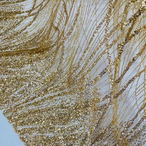 Puede incluir: Tela de brillo dorado con un patrón ondulado. La tela es transparente y tiene una textura delicada.