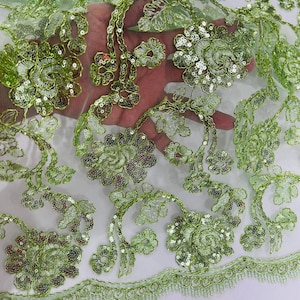 Könnte beinhalten: Grüner, mit Pailletten besetzter, floraler Spitzenstoff mit einem gewellten Rand. Die Spitze hat ein zartes Blumenmuster mit Pailletten und Perlen.