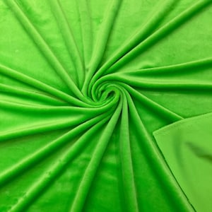 Op de afbeelding: Een felgroene stoffen achtergrond met een zachte, fluweelachtige textuur. De stof is gevouwen en gedrapeerd, waardoor een glad, vloeiend oppervlak ontstaat.