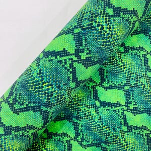 Puede incluir: Una tela enrollada con un vibrante estampado de piel de serpiente. El diseño presenta una mezcla de escamas verde brillante, amarillo-verdoso y verde azulado oscuro, creando un efecto visual llamativo. El material parece flexible y adecuado para diversos proyectos de manualidades.