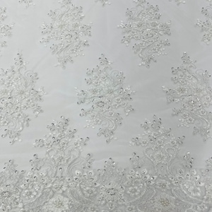 May include: White beaded lace fabric with a delicate floral pattern. The lace has a scalloped edge and is perfect for adding a touch of elegance to any project.