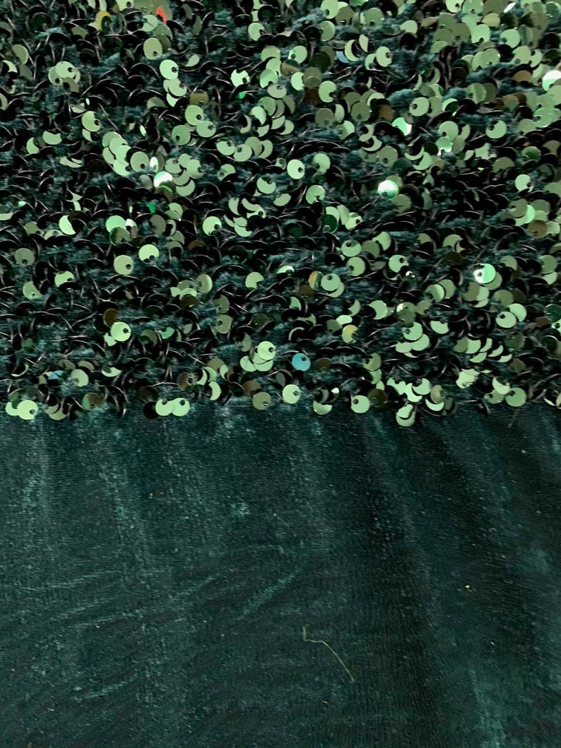 May include: A dark green fabric with a layer of green sequins on top. The sequins are arranged in a random pattern.