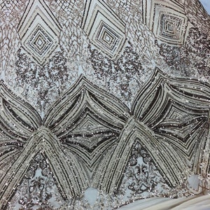 May include: A close-up of a gold and silver sequined fabric with a geometric pattern. The fabric is made of a sheer mesh material and is decorated with sequins and beads.