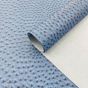 Puede incluir: Un rollo de cuero sint&eacute;tico azul con una superficie texturizada y con hoyuelos, que se asemeja a la piel de avestruz. El material est&aacute; parcialmente enrollado, revelando un reverso blanco. La apariencia general sugiere un material artesanal o de tapicer&iacute;a.