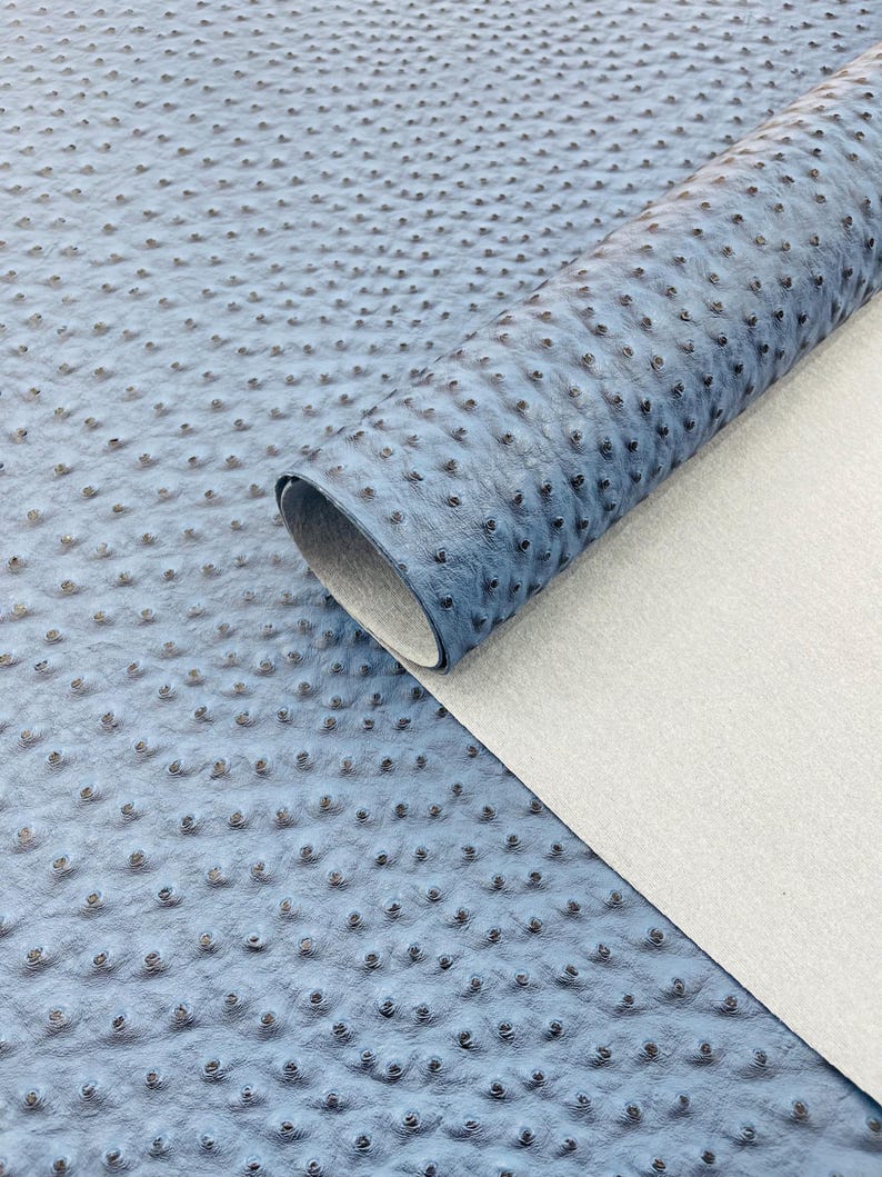 Puede incluir: Un rollo de cuero sint&eacute;tico azul con una superficie texturizada y con hoyuelos, que se asemeja a la piel de avestruz. El material est&aacute; parcialmente enrollado, revelando un reverso blanco. La apariencia general sugiere un material artesanal o de tapicer&iacute;a.