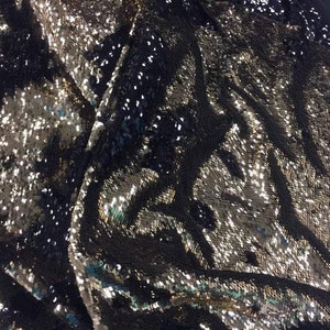 May include: Close-up of a black fabric with silver sequins. The sequins are arranged in a pattern that creates a shimmering effect.