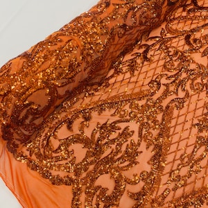 May include: Orange sequined fabric with a damask pattern. The sequins are scattered throughout the fabric, creating a shimmering effect.