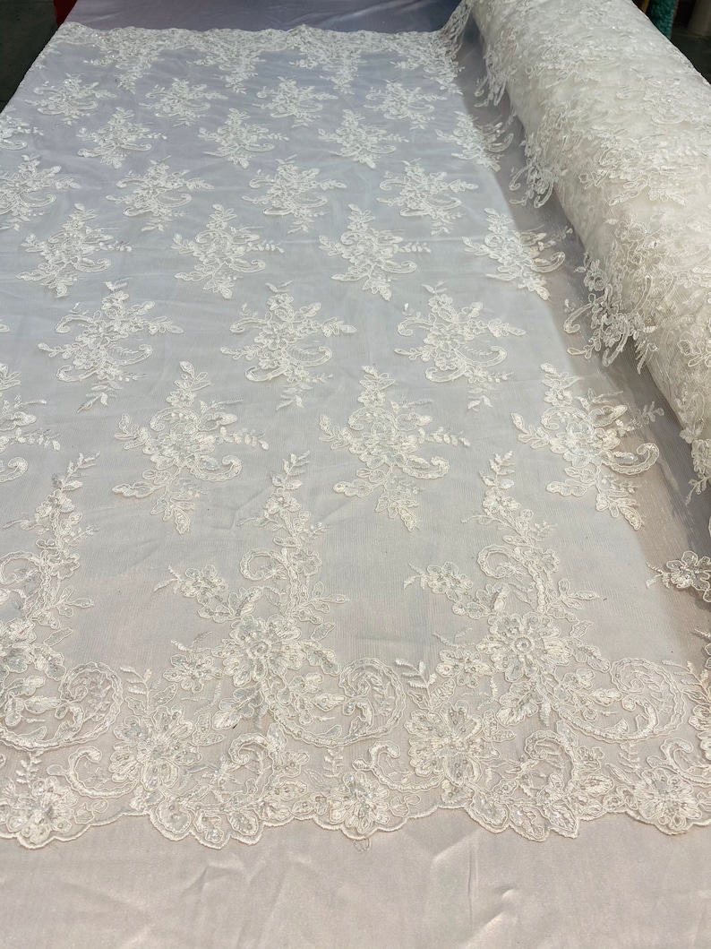 May include: White floral lace fabric with a delicate pattern. The lace is on a mesh background and has a scalloped edge.